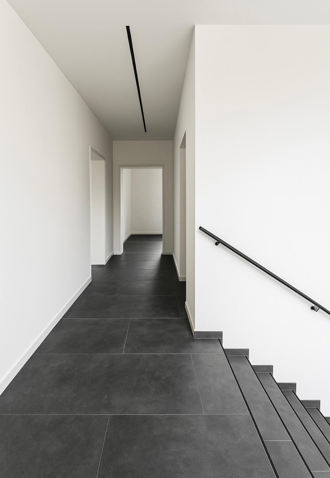 Treppenhaus mit anthrazitfarbenen Großformatfliesen und schwarzem Handlauf